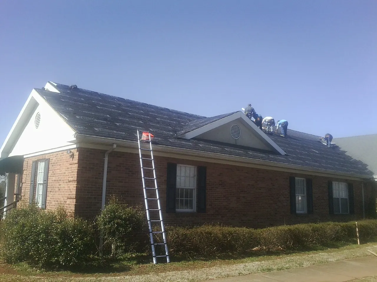 Crew tearing shingles off a brick ranch roof with a ladder set — Emergency Roof Repair work by our crew in Tarrytown