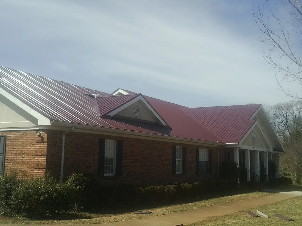 Red metal roof with gabled entries on a long brick building, from a Hail Damage Roof Repair job in Tarrytown