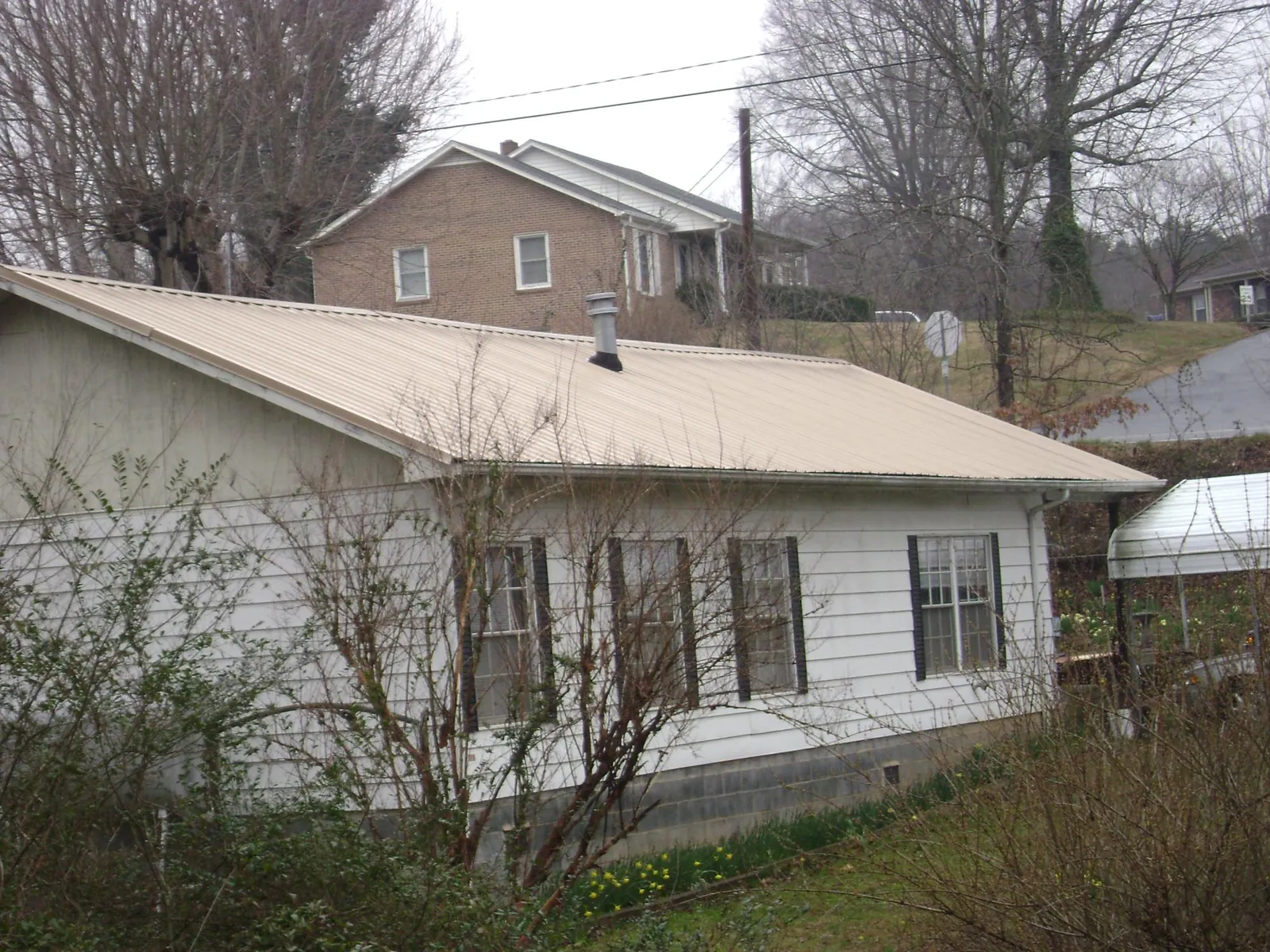 Tan metal roof on a white sided house set into a hillside — Commercial Roofing by Roofing Brothers in Tarrytown